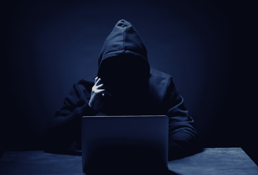 Spyware specialist in dark hoodie at computer – shady hacker representing a top hacking specialty