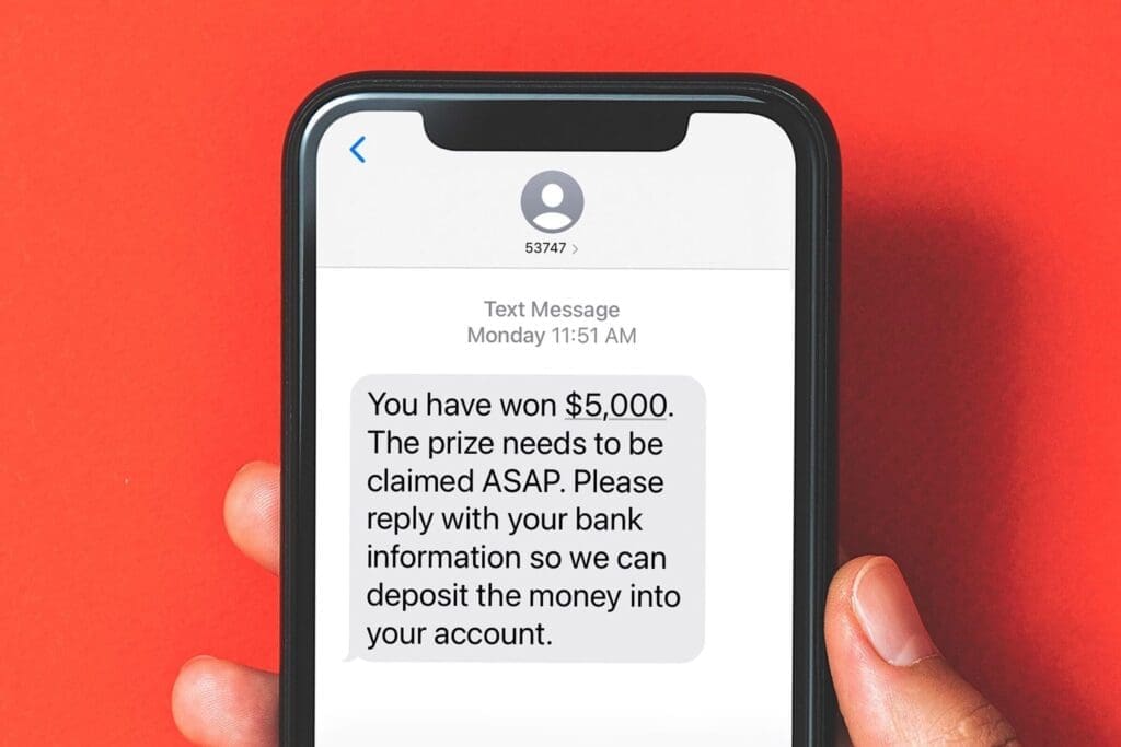 A person holding a smartphone, reading a text message that claims they’ve won $5,000 and must urgently reply with their bank account information to receive the prize—an example of a smishing scam.