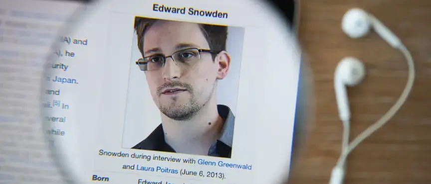 Edward Snowden, wearing glasses and a collared shirt, looking directly at the camera with a serious expression—known for leaking classified NSA documents in 2013.