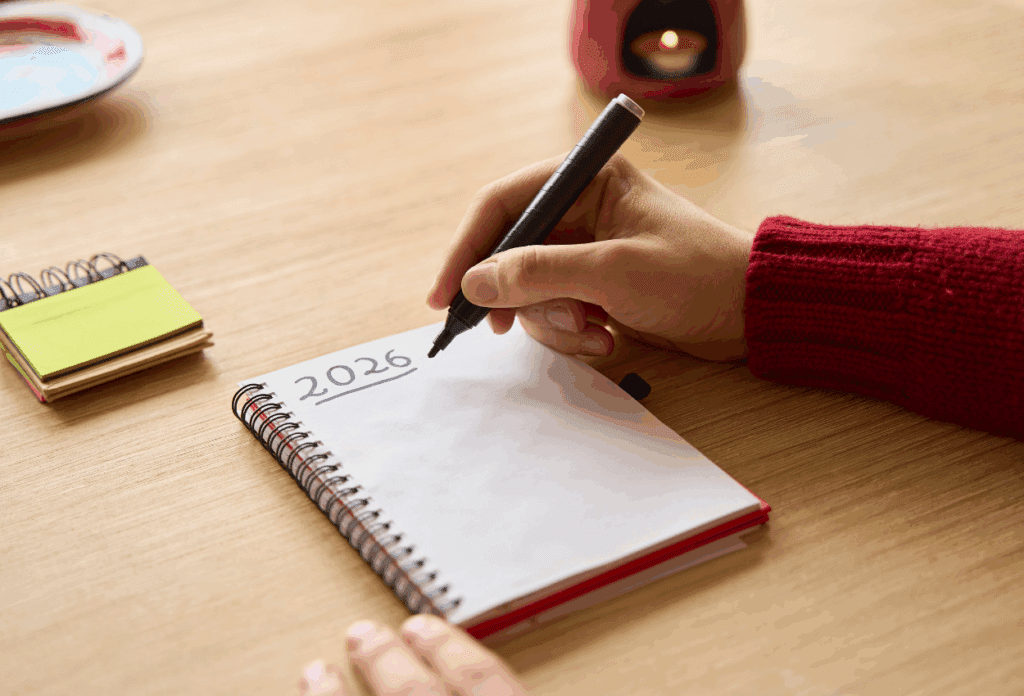 Person writing "2026" in a notebook, representing a cybersecurity checklist for future planning against phishing scams and ransomware attacks.