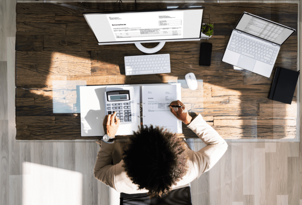 Overhead view of an accounting professional reviewing invoices and financial records at a modern workstation, representing the growing concern around accounting firm data breaches and the need for stronger cybersecurity protections.